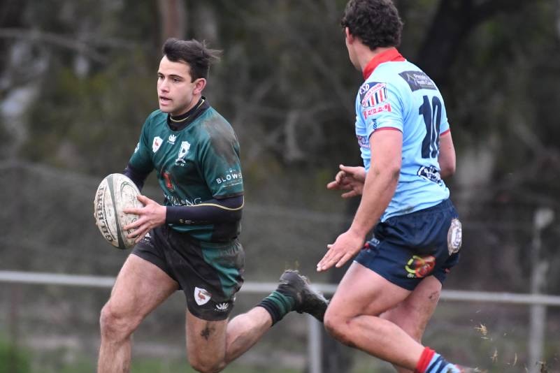 A rugby player in a green jersey running with the ball and being chased by an opposition player in a blue jersey