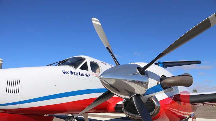An RFDS plane named 'Geoffrey Carrick' on the tarmac under blue skies.