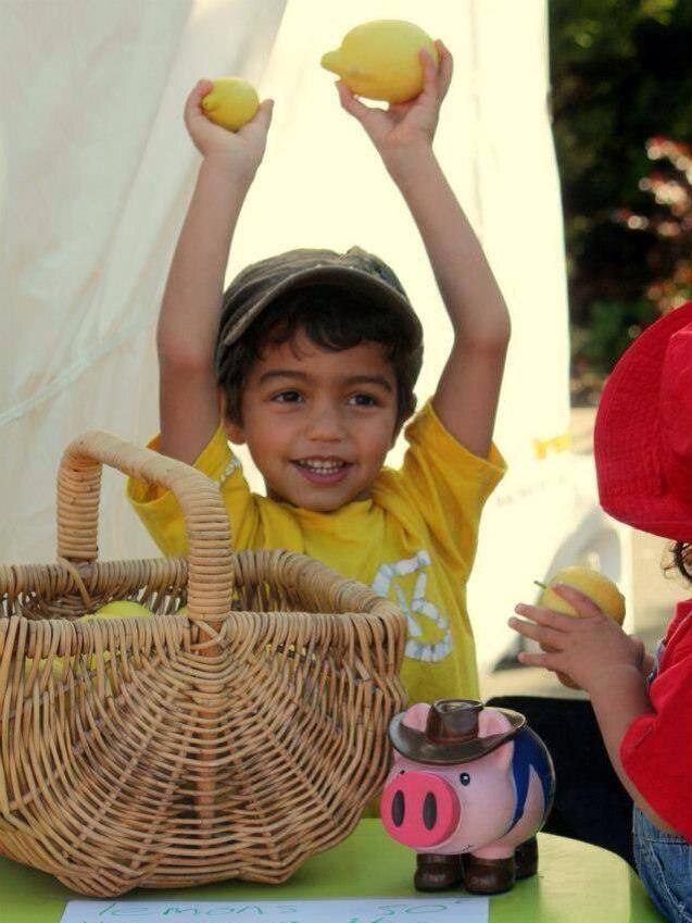 A smiling young boy holding up two lemons above his head.
