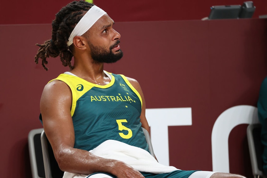 Australian basketballer patty mills sits on a chair with a towel looking like he is about to cry