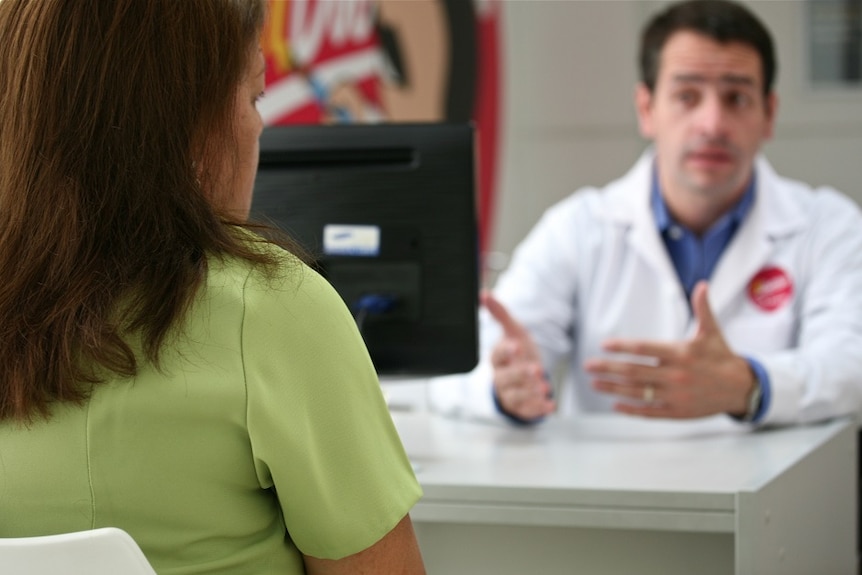 Man in white doctor's coat speaking to woman whose face can't be seen.