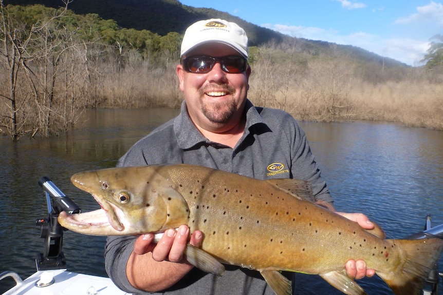 Wesley Chandler stands on a boat holding a large fish and smiling at the camera.