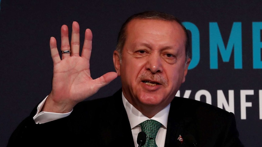 Turkish President Tayyip Erdogan holds up his hand during a speech.