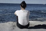 A woman sits on the cliff at Bondi Beach, looking out to the water.