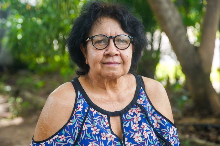 A woman with black hair, glasses and a colourful blouse.