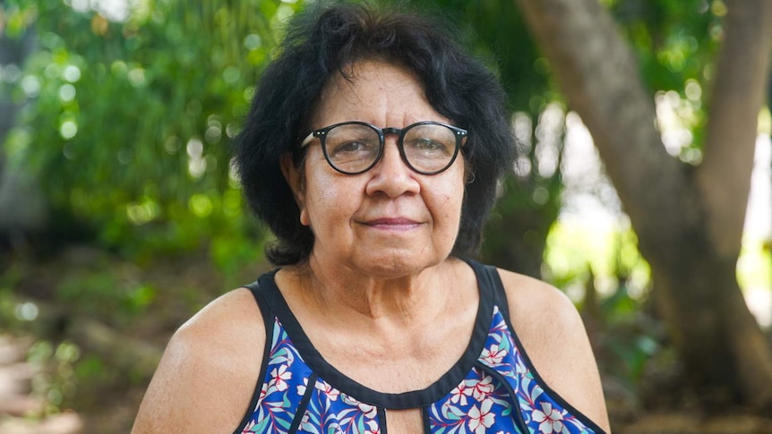 A woman with black hair, glasses and a colourful blouse.