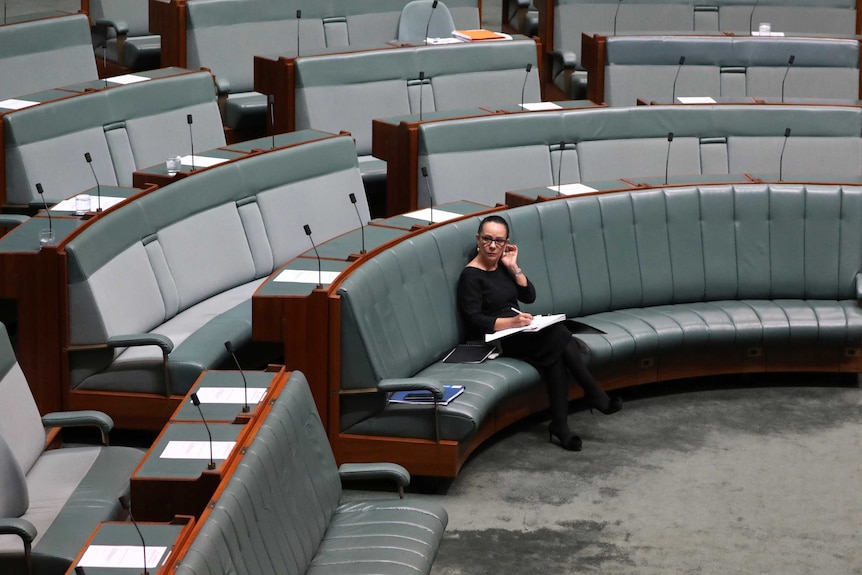 Linda Burney sits on the frontbench, with no other MPs around her. She's wearing black and looking through paperwork.