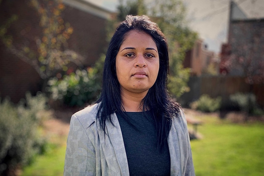 Dr Shalini Arunogiri stands in front of a garden backdrop and looks seriously into the camera.