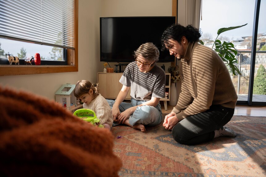 A young man and woman watch a toddler play with toys in a lounge room