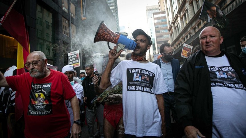 a crowd walking down a street, a man carries and yells into a megaphone