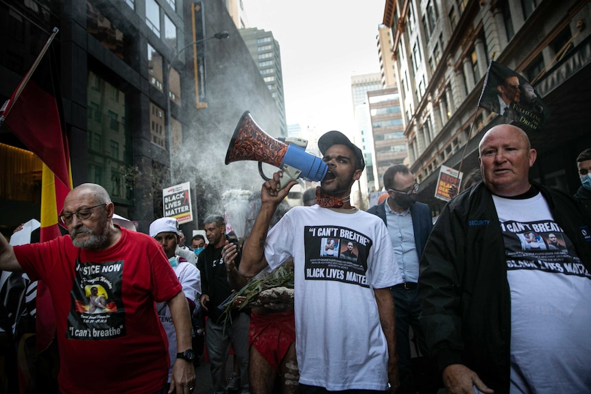 a crowd walking down a street, a man carries and yells into a megaphone