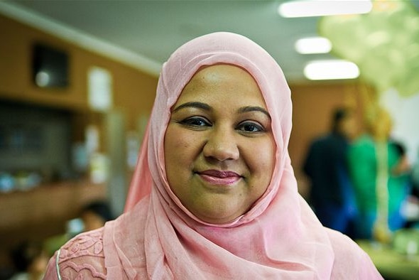 A Muslim woman wearing a light pink hijab, smiling at the camera.