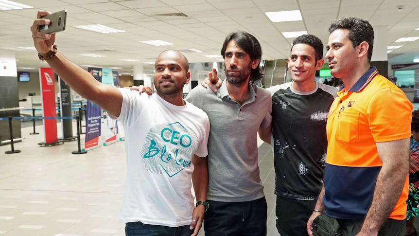 Four men have their photo taken on a mobile phone inside an airport terminal.