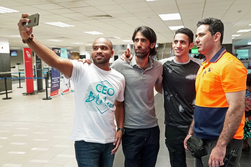 Four men have their photo taken on a mobile phone inside an airport terminal.