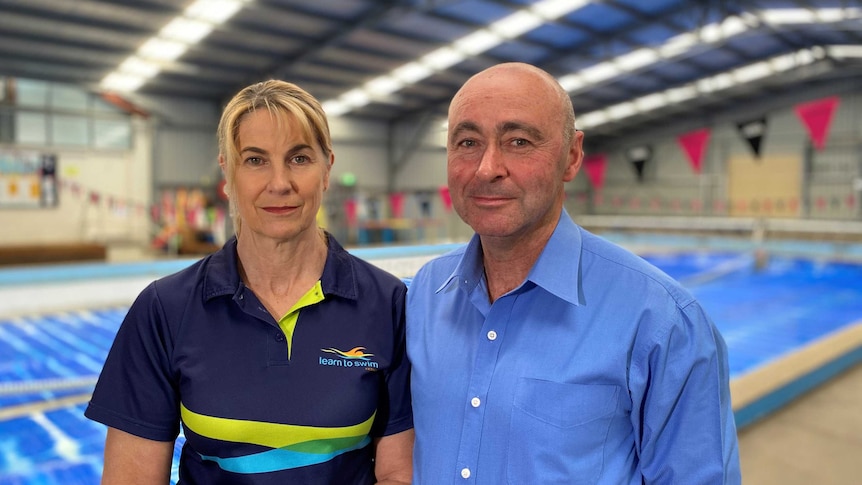 Joanne Love and Pasquale Di Iorio look at the camera in front of an indoor swimming pool.