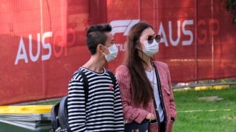A man and woman wearing surgical masks stand outside at the Australian F1 Grand Prix.