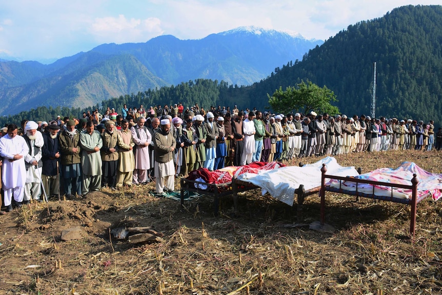 A large group of men attend the burial on a hilltop for three people killed