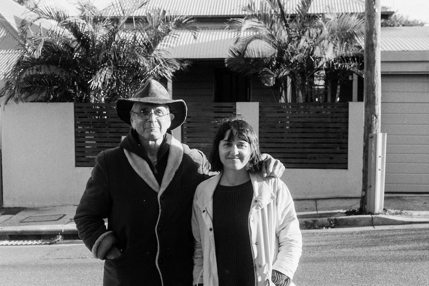 Monochrome of father hugging grown-up daughter on a street looking at camera.