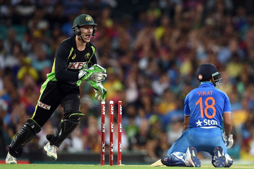 Australia's Cameron Bancroft reacts to stumping India's Virat Kohl during a T20 cricket match with Kohli kneeling on the ground.