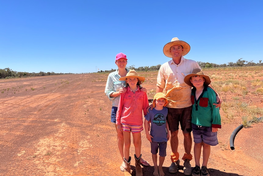 A woman and man with three children stand on a dirt outback airstrip
