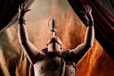 A circus perform on stage, with a sword down his throat and arms raised.