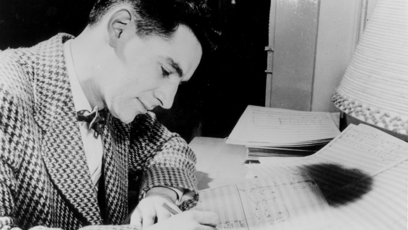A black and white photograph of Leonard Bernstein composing
