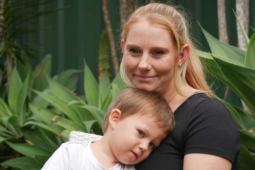 A women sits in backyard with a toddler on her lap.