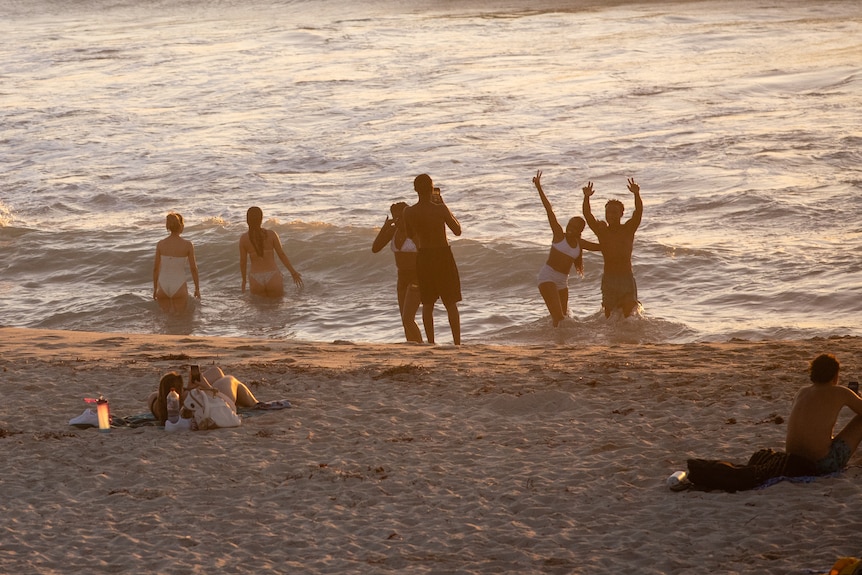 Members of the public at a crowded beach during sunset.