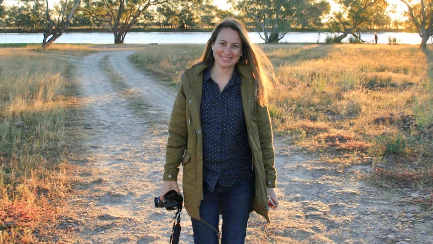 A woman with a camera, standing in a rural landscape.