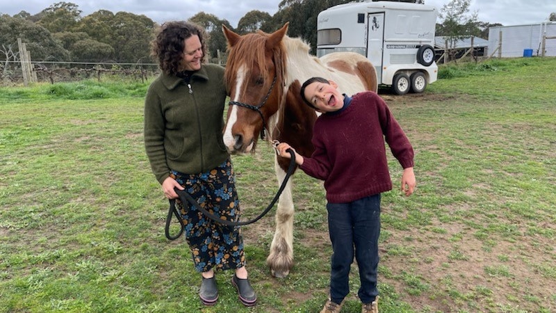 A woman holding a horse with a 12 year old boy next to the horse
