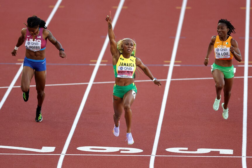 A Jamaican sprinter points her finger to the sky in triumphs as she crosses the line to win a 100m world title.