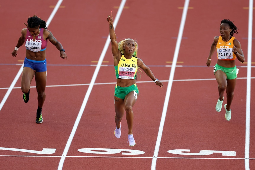 A Jamaican sprinter points her finger to the sky in triumphs as she crosses the line to win a 100m world title.