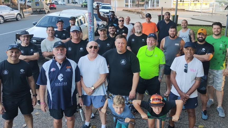 a group of 20 men of different ages wearing sports gear getting ready to walk along a street in Darwin
