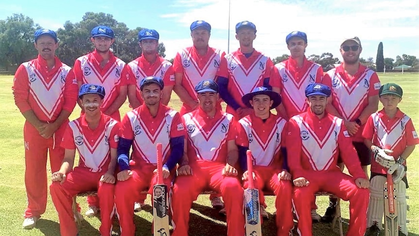 A group of cricketers wearing pink kits and blue caps pose for a photograph.