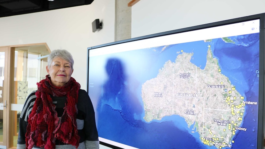 Lyndall Ryan stands next to a screen showing a map that plots massacres of Aboriginal people in the Frontier Wars.