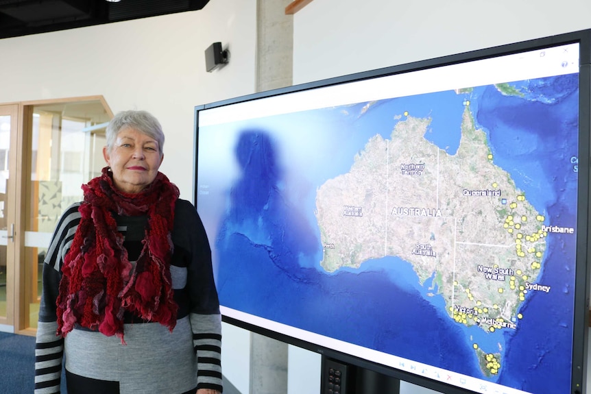 Lyndall Ryan stands next to a screen showing a map that plots massacres of Aboriginal people in the Frontier Wars.
