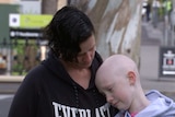 A child with a bald head rests it on a woman with black hair