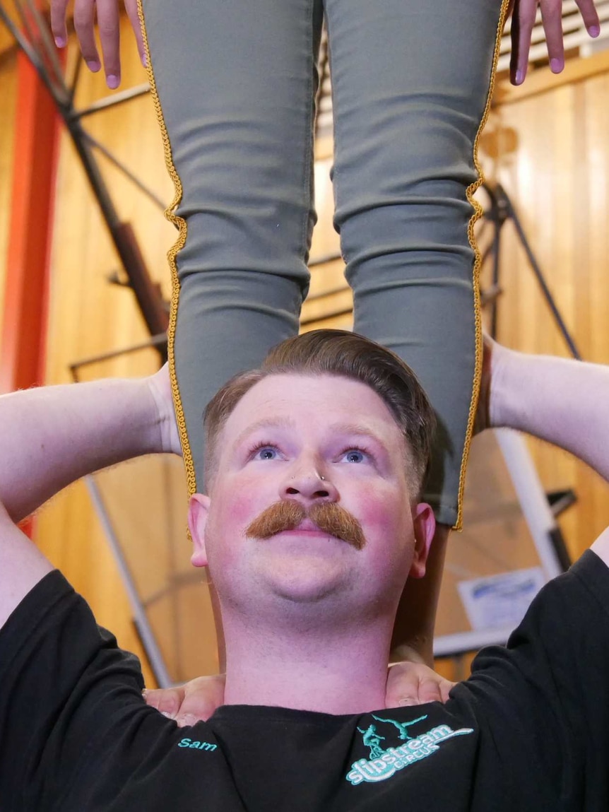 Sam Ladiges holds the legs of another circus performer.