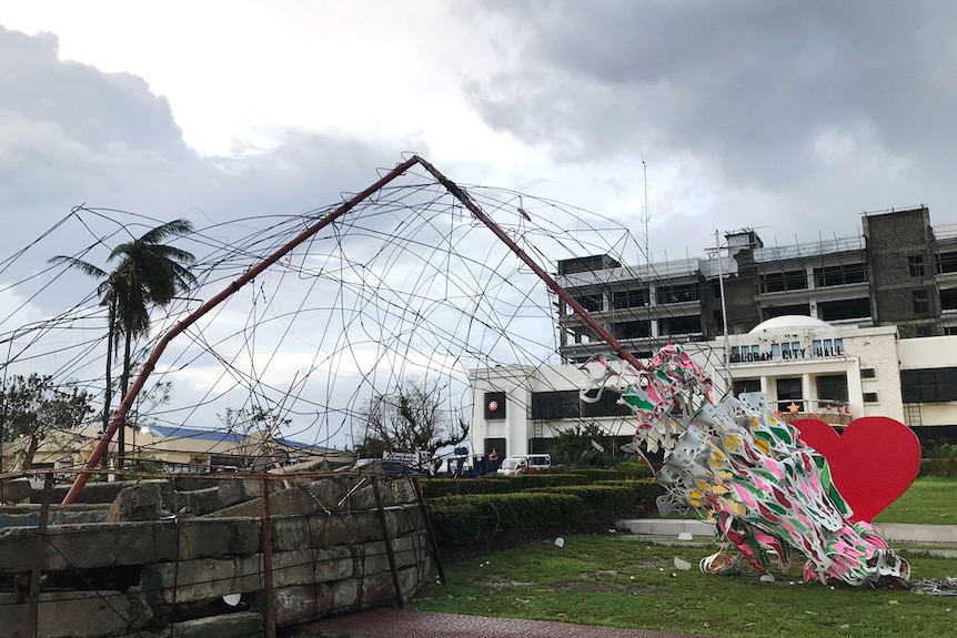 The skeleton of a large Christmas tree is shown bent over in front of a white two-storey city hall.