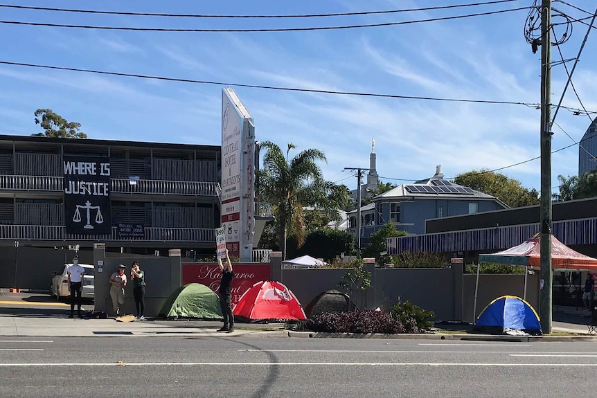 Refugee activists holding placards to cars on a busy road outside an apartment building