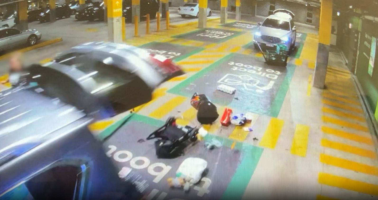 CCTV footage showing the back of a car, with the tailgate up, gorceries and a pram can be seen scattered on the ground