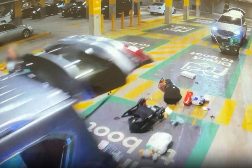 CCTV footage showing the back of a car, with the tailgate up, gorceries and a pram can be seen scattered on the ground