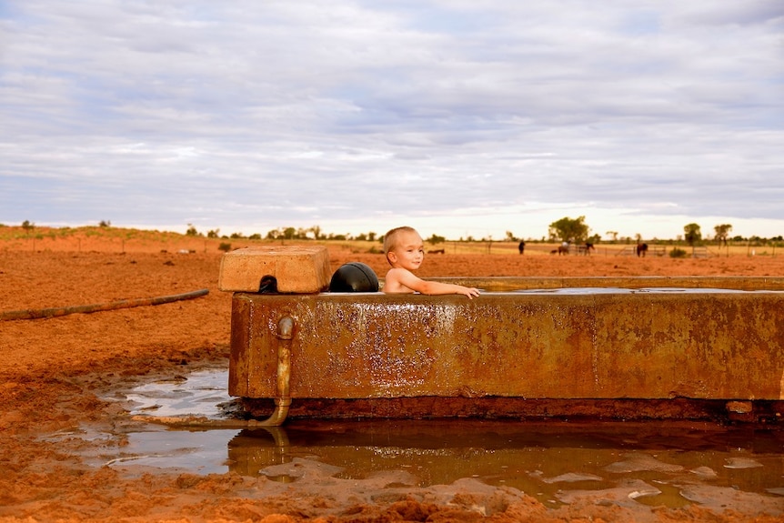 A little boy sits in a full cattle trough after rain in the Channel Country