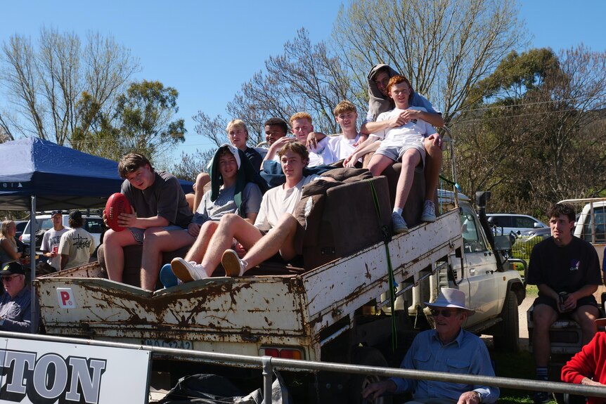 A group of young men sit on the couches put in  the back of a ute.
