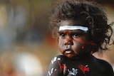 Close-up of Indigenous toddler, smiling, with coloured paint across their face.