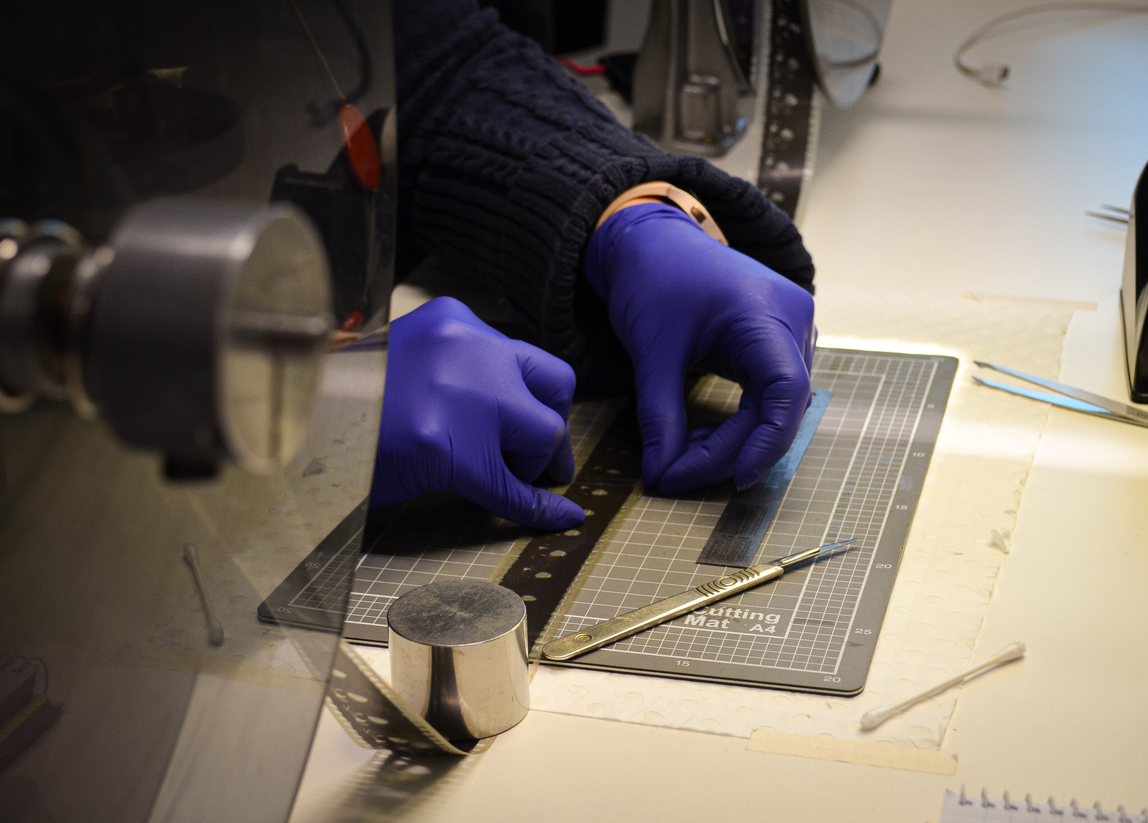 Tape is being carefully applied to the reel, with scalpels lying next to the reel where the tape has been cut