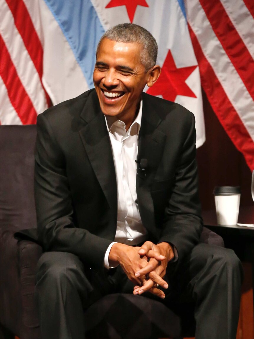 A smiling Barack Obama sits with his hands folded after returning to the stage in Chicago.