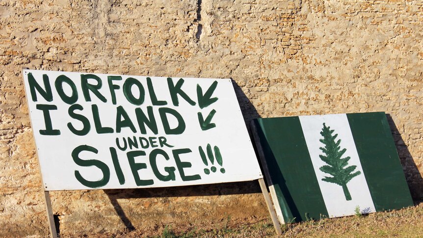 A sign resting on Norfolk Island's prestigious Quality Row reads 'Norfolk Island under seige'.