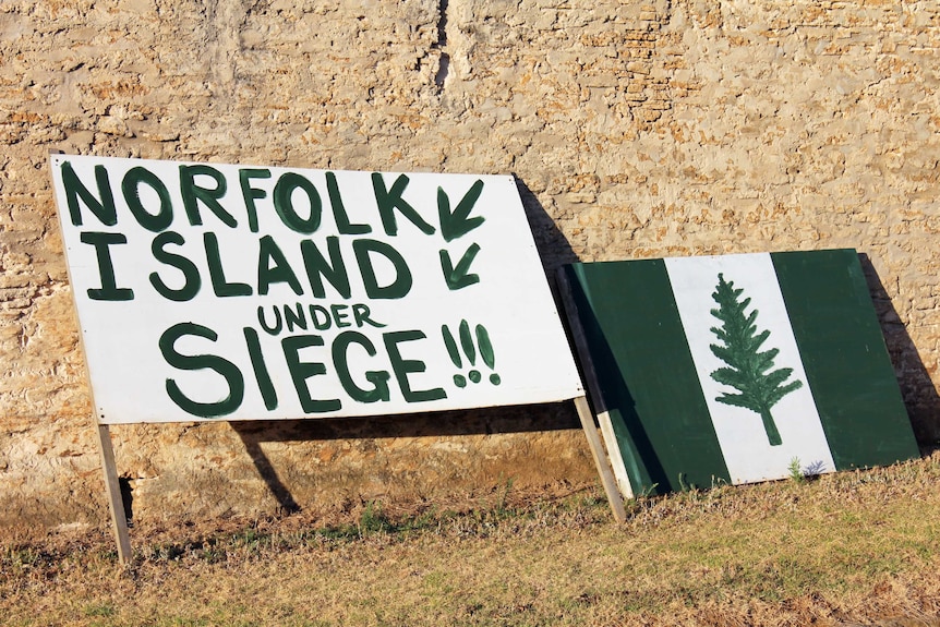 A sign resting on Norfolk Island's prestigious Quality Row reads 'Norfolk Island under seige'.