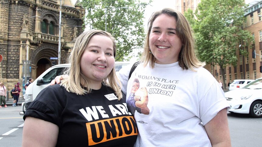 Kate and Nellie stand on the street wearing t-shirts bearing union slogans.